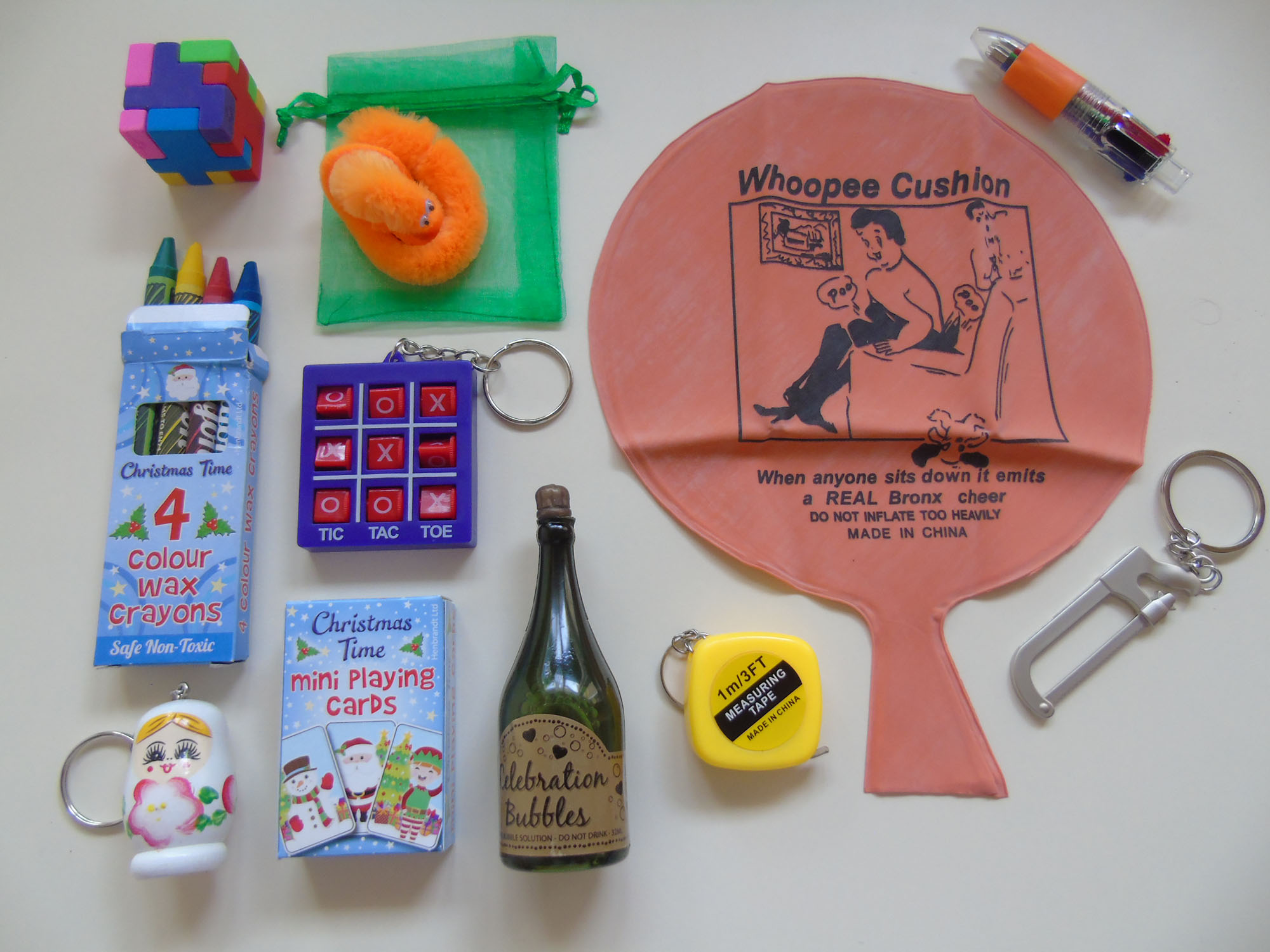 A collection of premium cracker gifts included inside House of Crackers Economy Christmas crackers, featuring mini Tic Tac Toe, mini metre tape measure, a whoopee cushion and eraser cube.