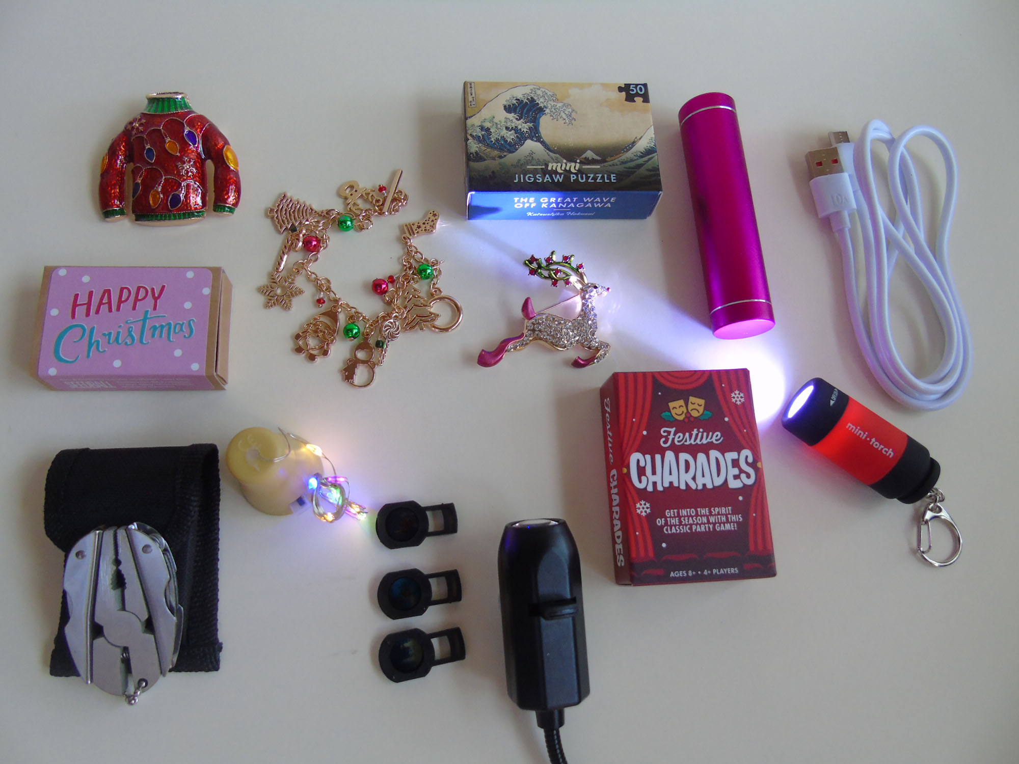 A collection of premium cracker gifts included inside House of Crackers luxury Christmas crackers, featuring metal pocket tools, elegant brooches, and silver cufflinks and a projector torch.