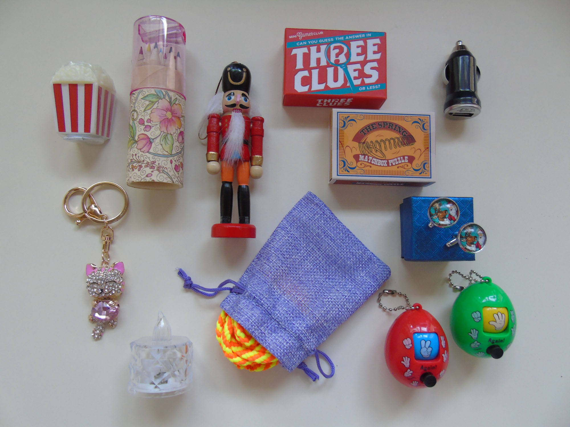 A collection of premium cracker gifts included inside House of Crackers Family Christmas crackers, featuring bling keyring, a wooden nutcracker ornament, enamel cuff links, rock, paper scissors game and mini puzzle game in a matchbox.